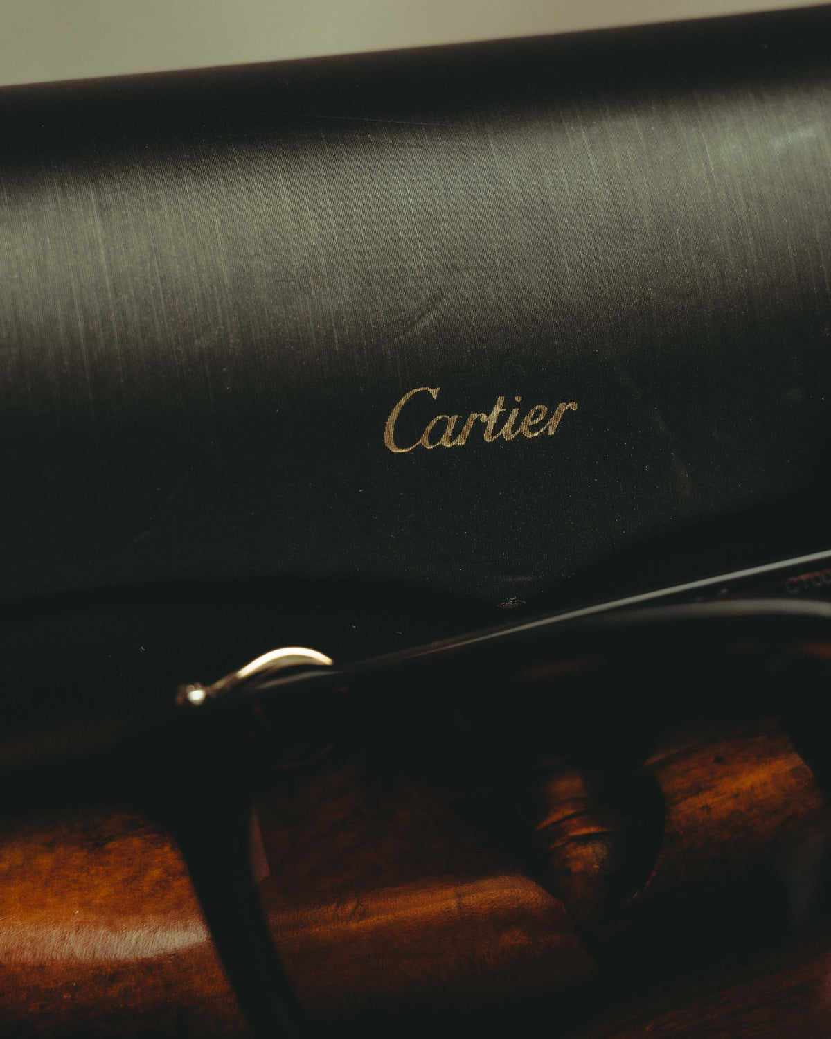 ダークブラウンのべっ甲調テンプルに配された筆記体のCartierロゴと、C字形ゴールドカラー金具を捉えたディテールカット。