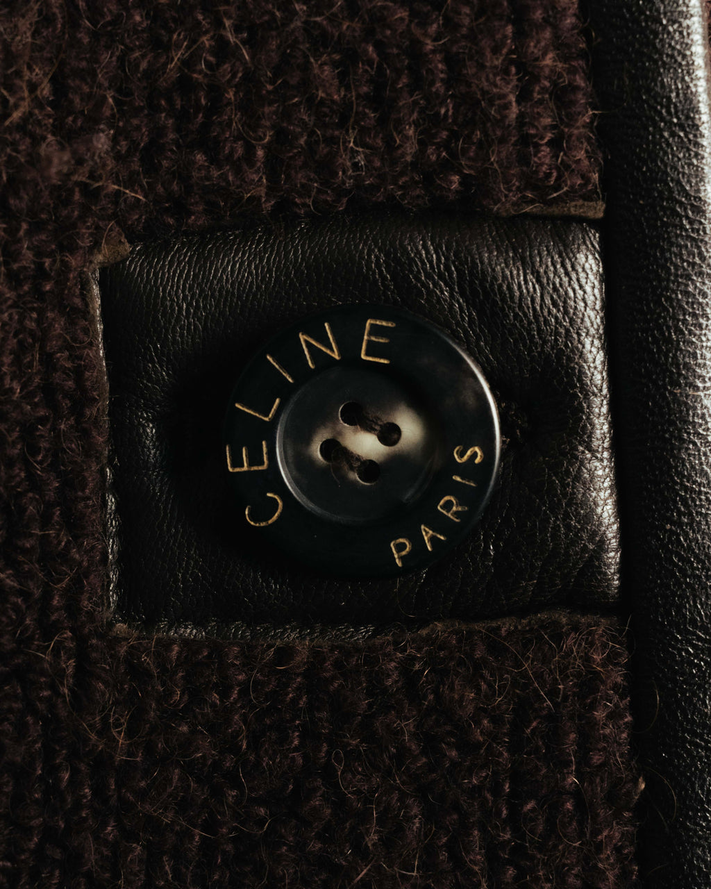 CELINE PARISの表記が刻まれた4穴ボタンを、ダークブラウンのレザー台座とともに捉えたディテールカット。起毛感のある本体生地とレザートリミングの異素材使いが確認できます。