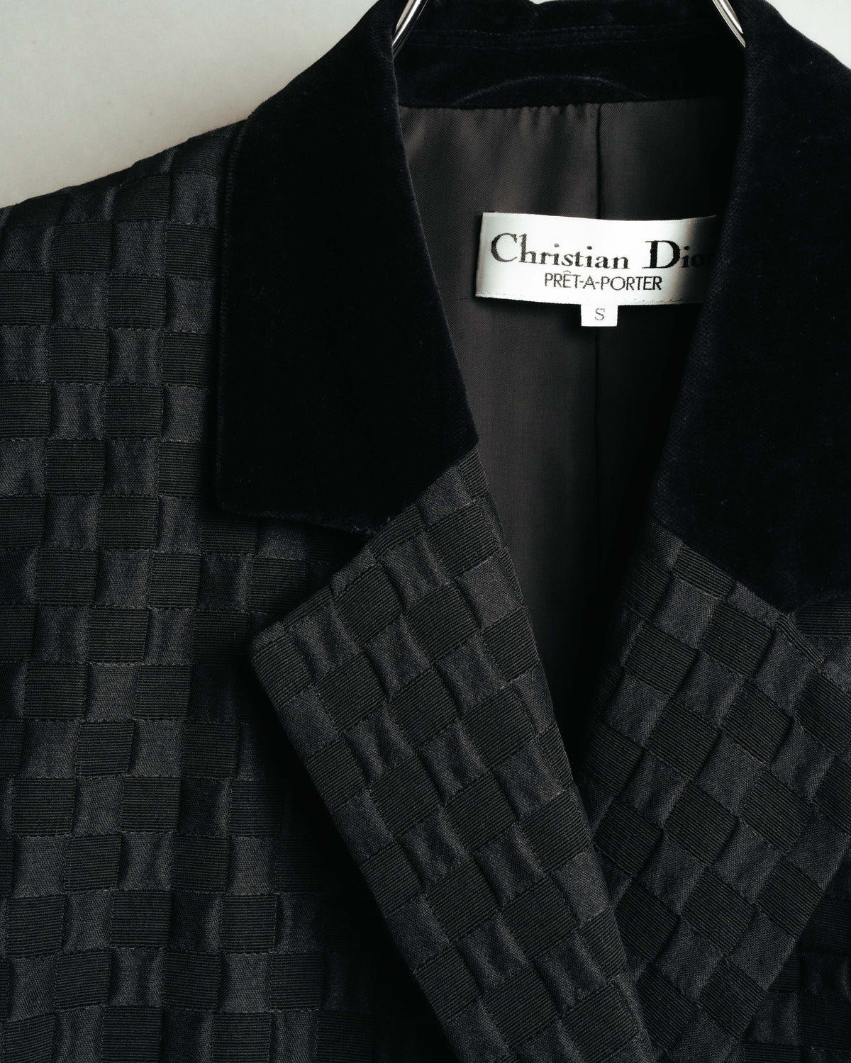 首元のChristian Dior PRÊT-À-PORTER織りネームとサイズ表記を確認できるカット。身頃の市松状ジャカード生地と、深く光を吸収するベルベット調の起毛襟の対比も捉えています。