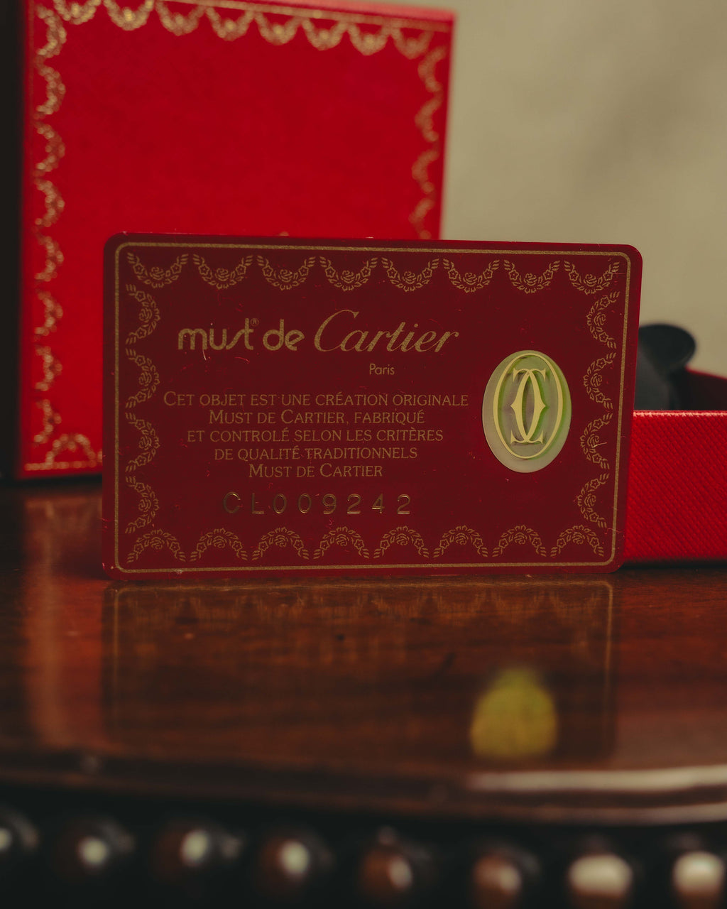 Must de Cartier Parisのロゴ、品質表記、シリアルナンバーが記された赤い保証カードのカット。付属品として、同時代のレザーアクセサリーの背景に言及する箇所と照合しやすい一枚です。