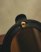 開いた内側のブラックレザー縁に配された、Cartier刻印入りゴールドカラーの留め具（スナップボタン）のアップ。円形ミラーの周囲を包むレザーと、円周に沿うステッチも確認できるカットです。