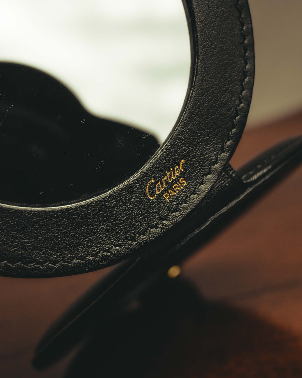 開いた内側のブラックレザーに配された、ゴールドカラーのCartier Parisロゴ刻印。円形ミラーの周囲を包むレザーと縁のステッチも確認できるカット。