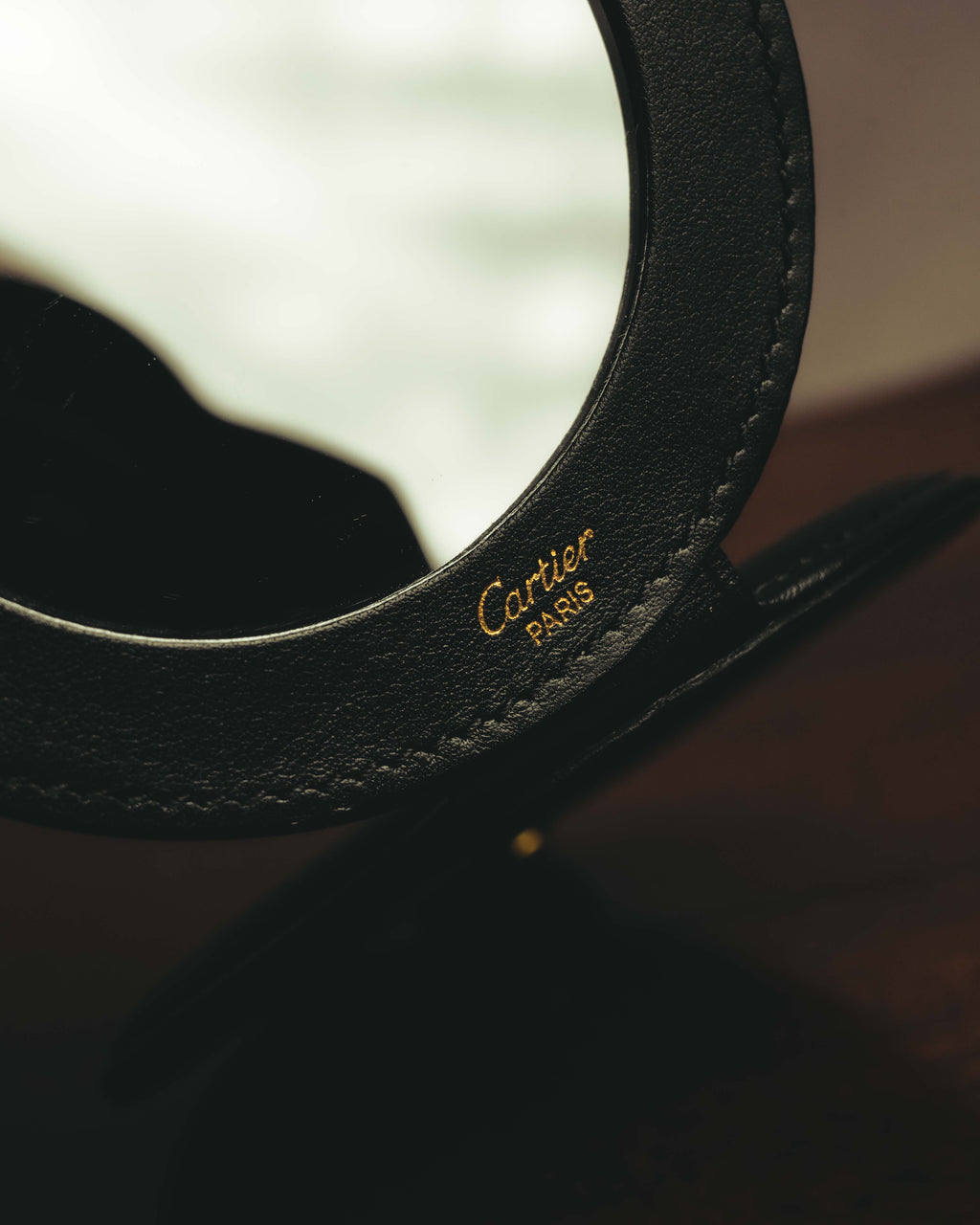 開いた内側の円形ミラーと、その周囲のブラックレザーに入るゴールドカラーのCartier Parisロゴを捉えたディテールカット。