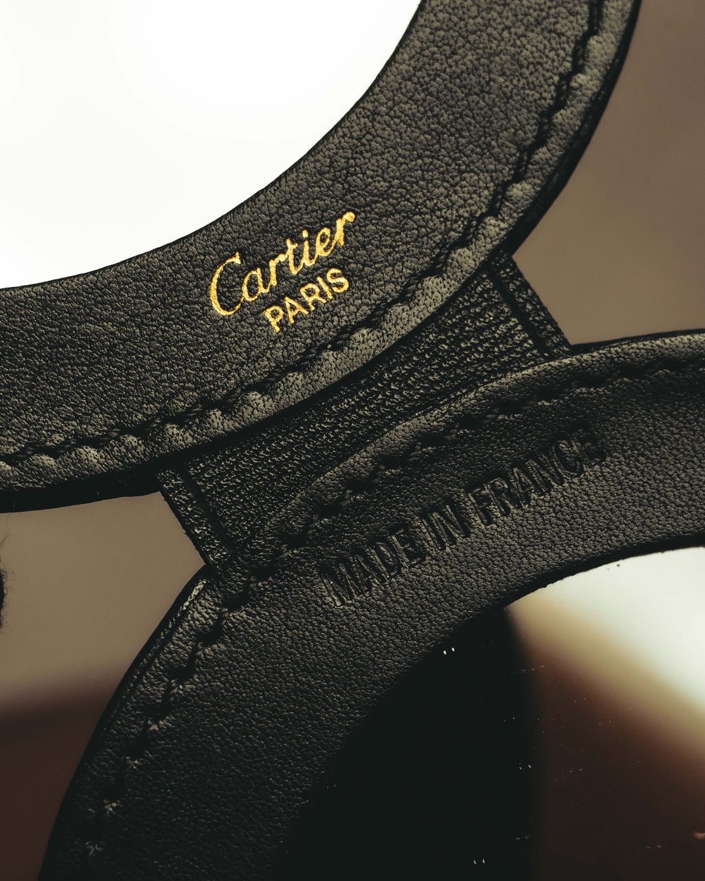 開いた内側のブラックレザーに施された、ゴールドカラーのCartier ParisロゴとMade in Franceの型押しを捉えたカット。円形ミラー周囲を包むきめ細かなレザーの表情も確認できます。