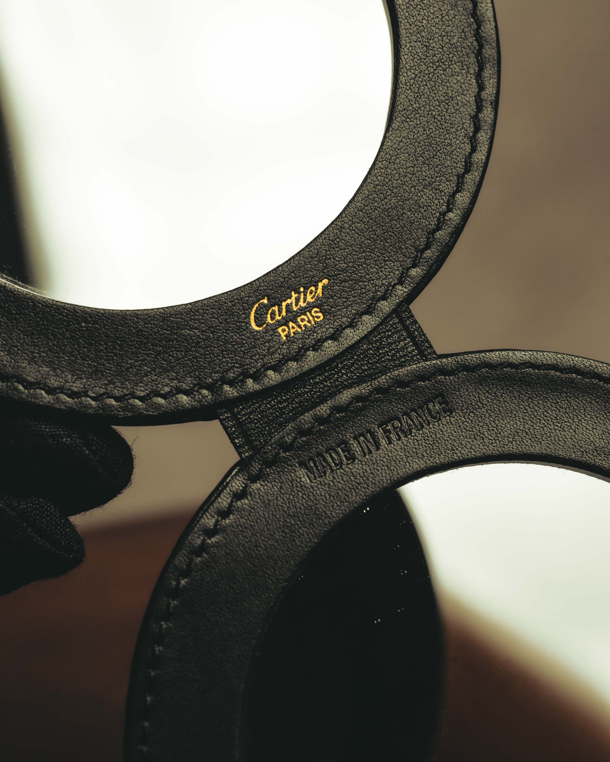 開いた二面ミラーの内側に配された、ゴールドカラーのCartier ParisロゴとMade in Franceの型押しを捉えたカット。ブラックレザーの縁取りと円周に沿うステッチも確認できます。