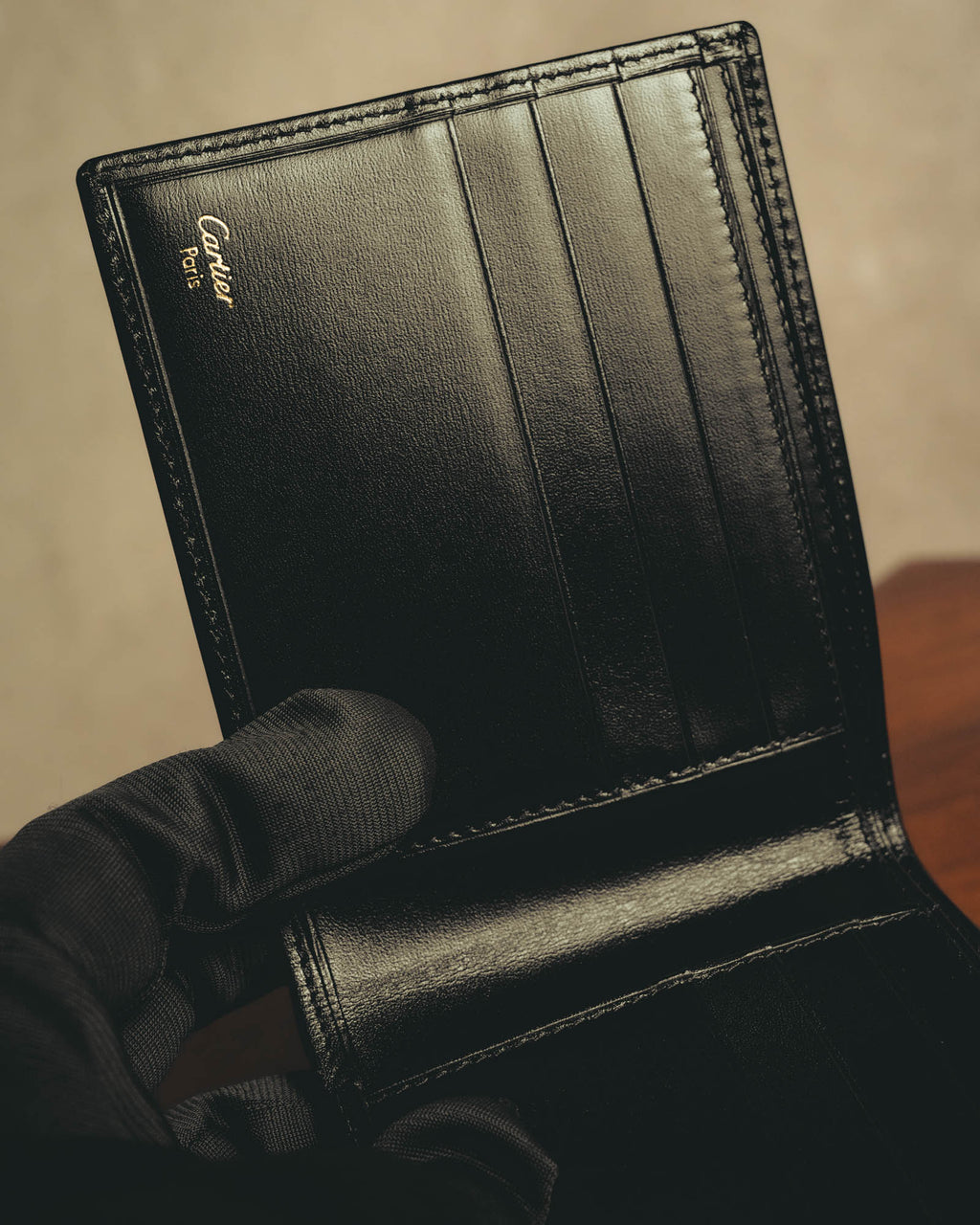 内装に施されたCartier Parisのゴールド箔押しと、複数のカードスロットを捉えたディテールカット。ブラックの革様素材と同色ステッチ、二つ折りの内装構造が確認できます。