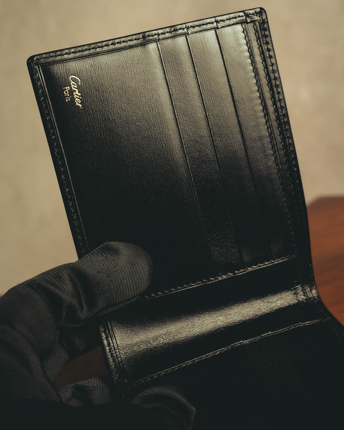 内装に施されたCartier Parisのゴールド箔押しと、複数のカードスロットを捉えたディテールカット。ブラックの革様素材と同色ステッチ、二つ折りの内装構造が確認できます。