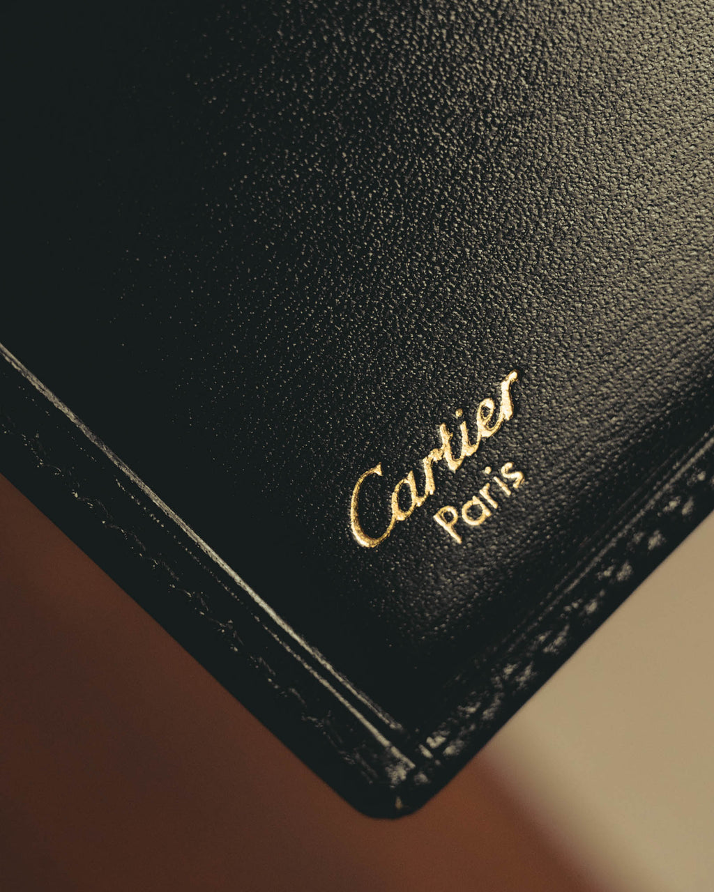 内装に施されたCartier Parisのゴールド箔押しと、縁に沿った同色ステッチを捉えたディテールカット。カードスロットの一部と細かなシボを備えた革様素材の表情が確認できます。