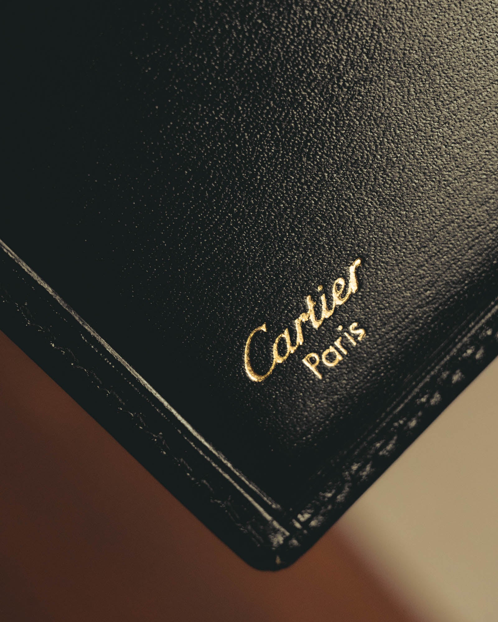 内装に施されたCartier Parisのゴールド箔押しと、縁に沿った同色ステッチを捉えたディテールカット。カードスロットの一部と細かなシボを備えた革様素材の表情が確認できます。