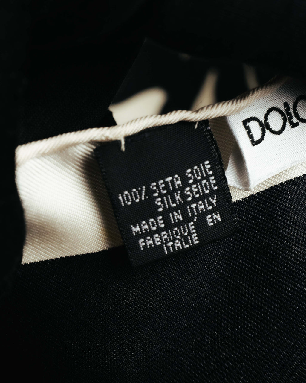 「100% SETA SILK」とイタリア製を示す表記が確認できる、黒地の素材・原産国表示タグのクローズアップ。隣にブランドネームタグの一部も写っています。