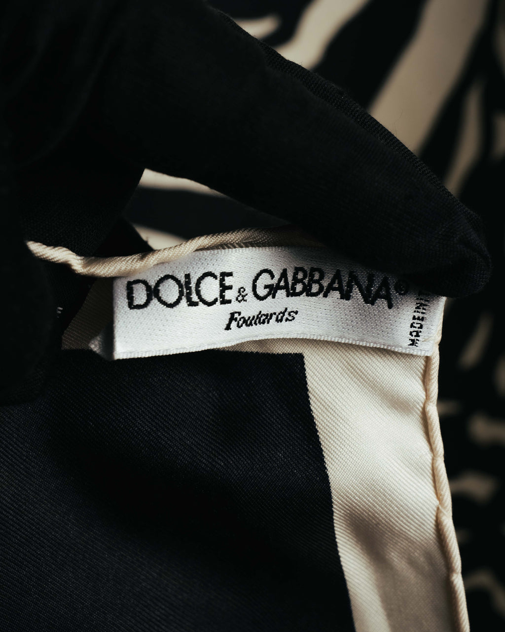ブランド名と「Foulard 85」の表記が確認できる白い織りタグのクローズアップ。ブラックのボーダーとアイボリー系のツイル調生地も写るディテールカット。