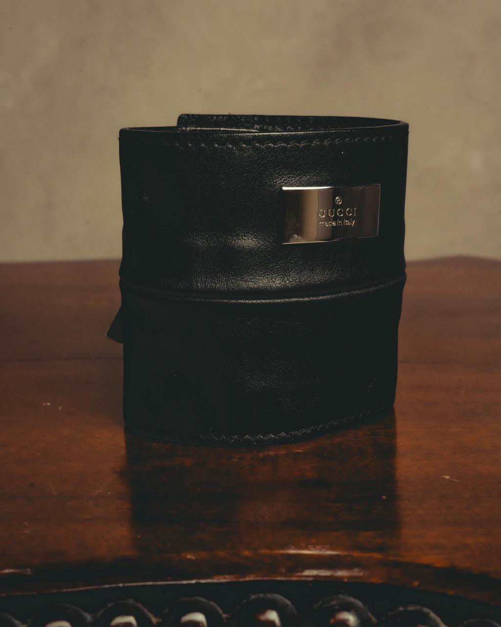 ブラックのワイドカフ正面に、GUCCIとmade in Italyの刻印を施した銀色のメタルプレートを配したカット。きめ細かなシボを備えたレザーと、立体的なジップポケットの輪郭も確認できます。