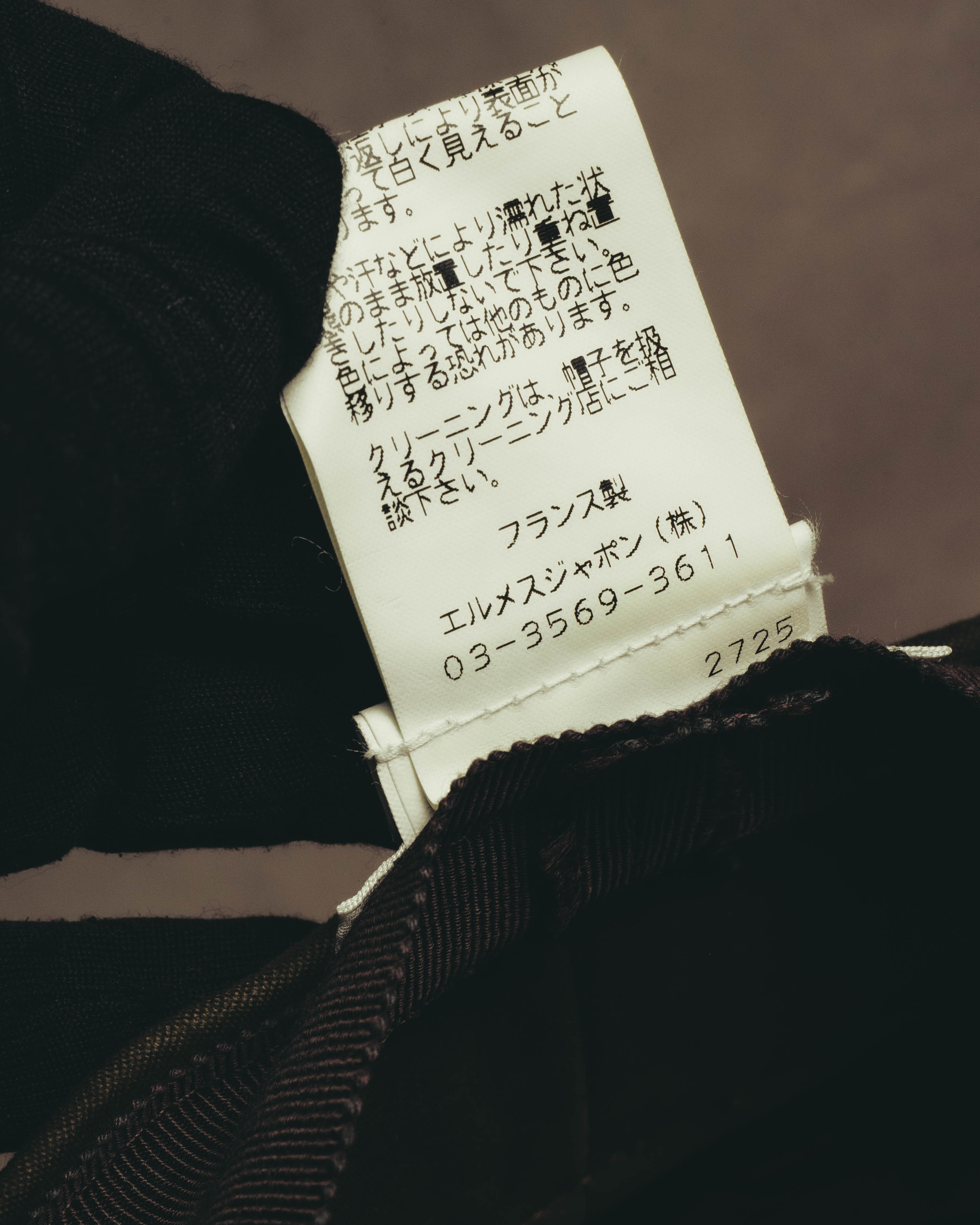 帽子内側に付属する品質表示タグのアップ。エルメスジャポン株式会社の東京03地域の電話番号と、旧JIS方式の洗濯記号に関わる表記を確認できるカット。