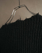 襟元に連続するクラッシュと不均一なフリンジを捉えたディテールカット。深いブラックの畦編みに、厚みと起毛感のある編地が確認できます。