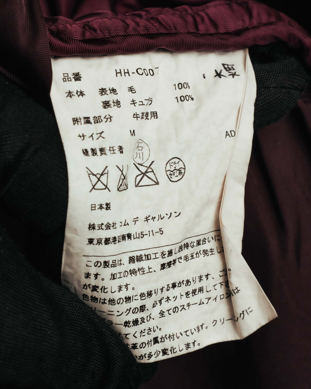 品番HH-C007、表地ウール100パーセント・裏地キュプラ100パーセント、付属部分牛革使用を記した内側の品質タグ。日本製および株式会社コム デ ギャルソンの表記も確認できるカット。