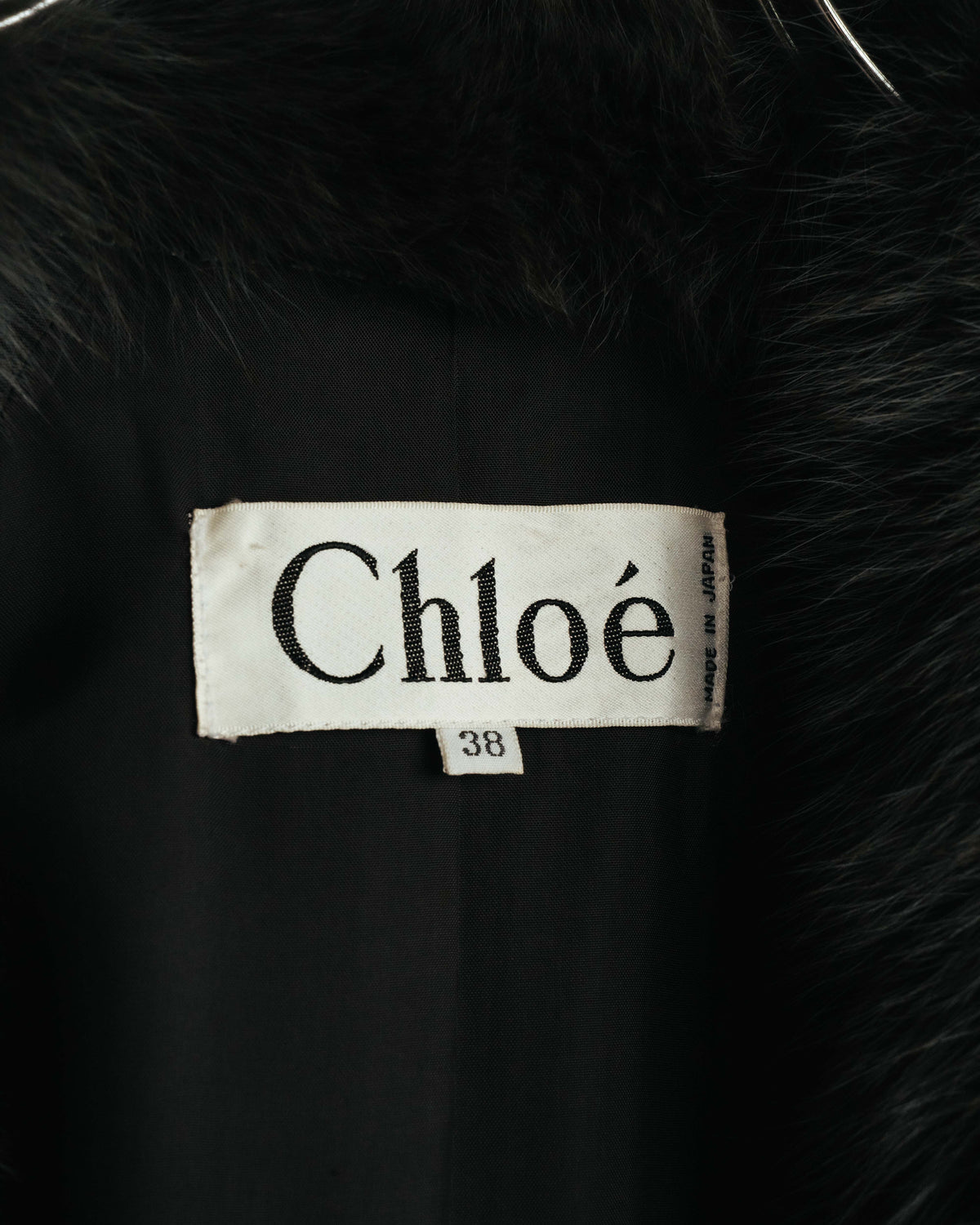 裏地側に配されたChloéのブランドネームタグと、サイズ38表記を確認できるカット。周囲にはファー状襟の毛足と滑らかなブラックの裏地が写されています。