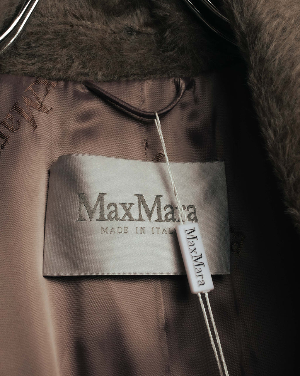 「Max Mara」「MADE IN ITALY」と表記された内タグのクローズアップ。ブランドロゴが繰り返し配された光沢のある裏地と、毛足のある表地の境目を確認できるカット。