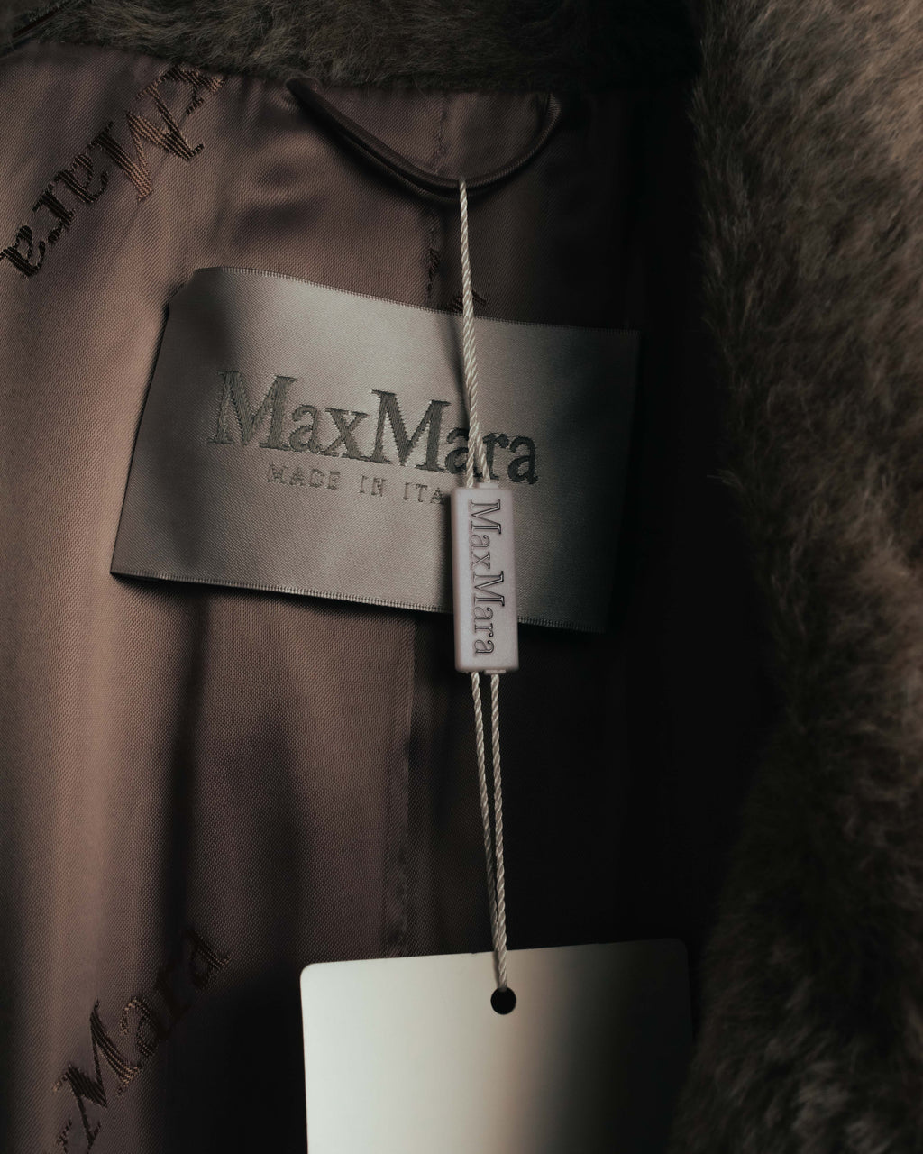 「Max Mara」「MADE IN ITALY」表記が読める内タグと、ブランドロゴが繰り返し配された光沢のある裏地のカット。首元付近には毛足のある表地も写っています。