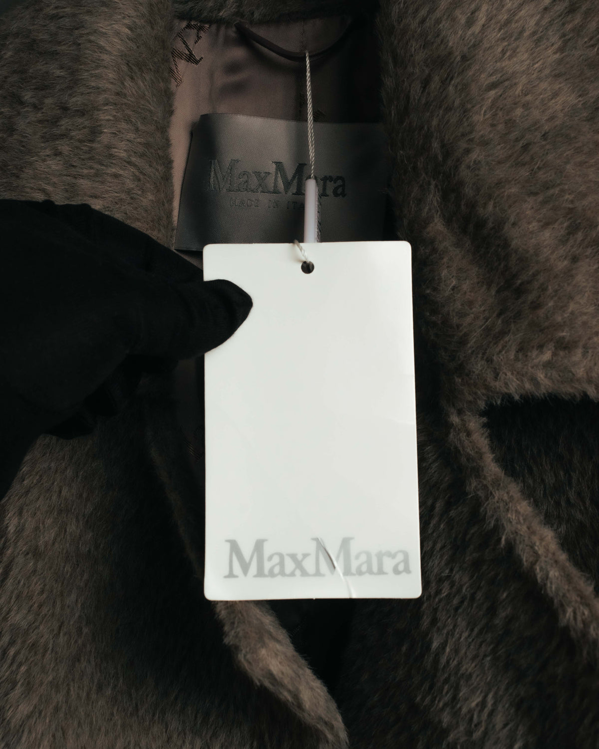 首元に配されたMax Maraロゴ入りのブランドタグと下げ札を捉えたカット。周囲には細やかな毛足が密集した表地が写っています。