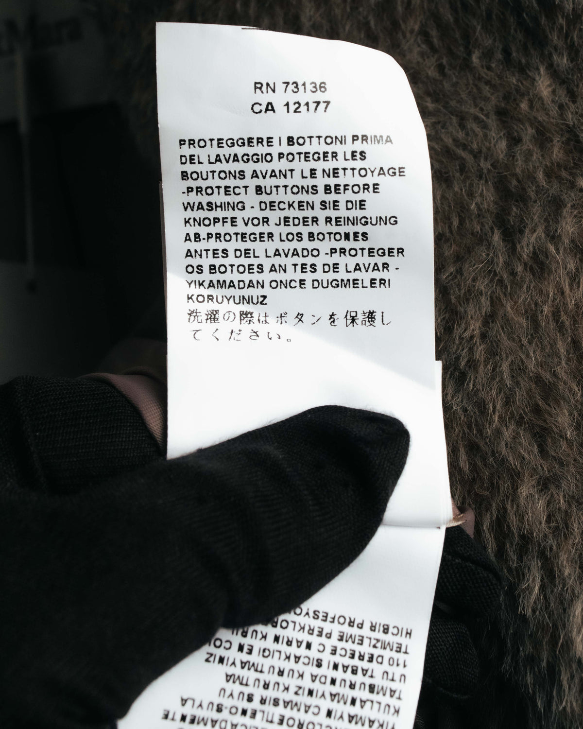 内側に配された洗濯表示タグのアップ。洗濯前にボタンを保護する旨が多言語で記載されています。