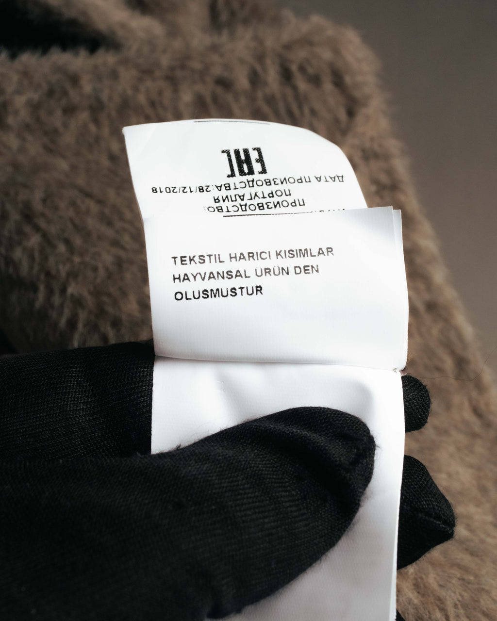コート内側の品質表示タグを写したカット。製造日として「28/12/2018」の表記と、動物由来素材に関する注意書きが確認できます。