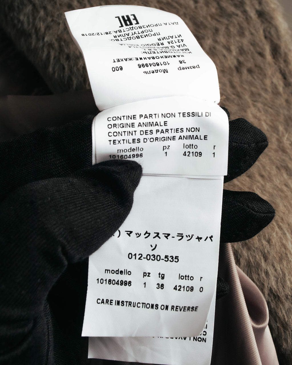 コート内側に付された品質表示タグと品番タグのクローズアップ。動物由来の非繊維部分に関する表記、モデル番号、サイズ表記を確認できるカット。