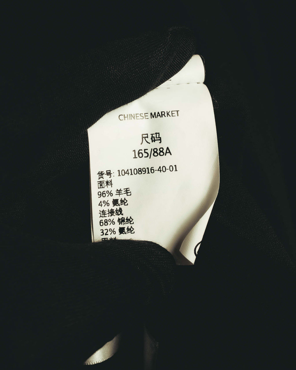 内側に配された中国語表記の品質表示タグを写したカット。表地の素材混率とサイズ表記「165/88A」が確認できます。