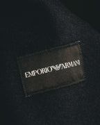 首元に配された、EMPORIO ARMANIの文字と白いイーグルロゴを記した黒地のブランドラベル。周囲には細やかな起毛感を備えた濃色の表地が写る。