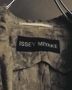 黒地に白いサンセリフ体で「ISSEY MIYAKE」を織り込んだネックタグのクローズアップ。周囲には顔料染めによる不均一な濃淡と皺の表情が見られます。
