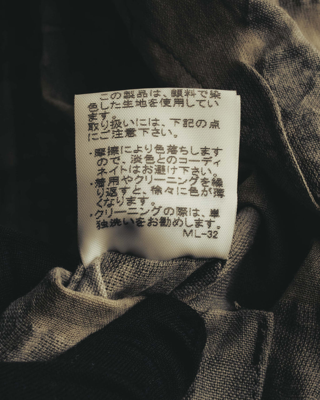 内側に配された品質表示タグのカット。色落ちやクリーニング時の注意書きが確認でき、顔料染めによる色調変化に関する記載を捉えています。