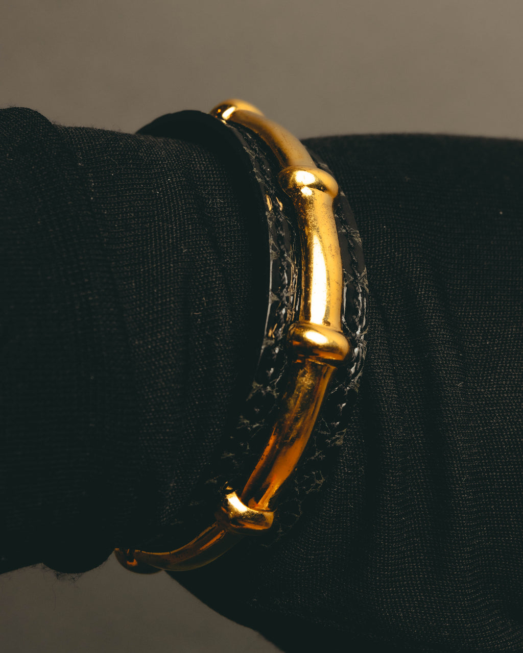 手首に着用した、節のある竹を思わせるゴールドトーンの金属パーツとブラックレザーのカフ。立体的な竹状パーツが手元に沿う様子を捉えたカット。