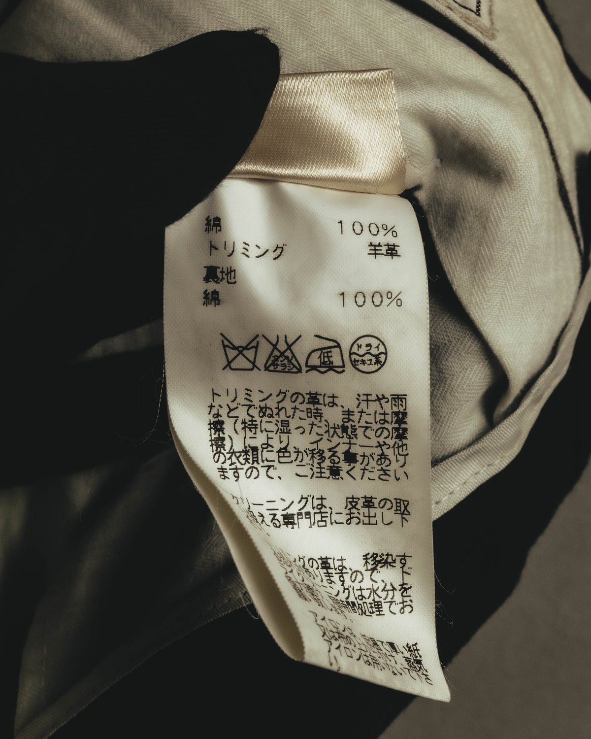 綿100％の本体と、羊革100％のトリミングを示す品質表示タグ。旧JIS洗濯表示と革トリミングの取り扱い注意書きが確認できる内側のカット。