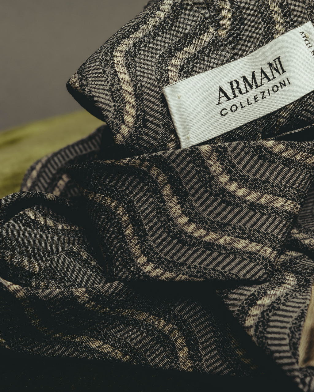 「ARMANI COLLEZIONI」表記のブランドタグと、細かな斜行した織りの上に柔らかく蛇行するラインを重ねた生地を捉えたカット。