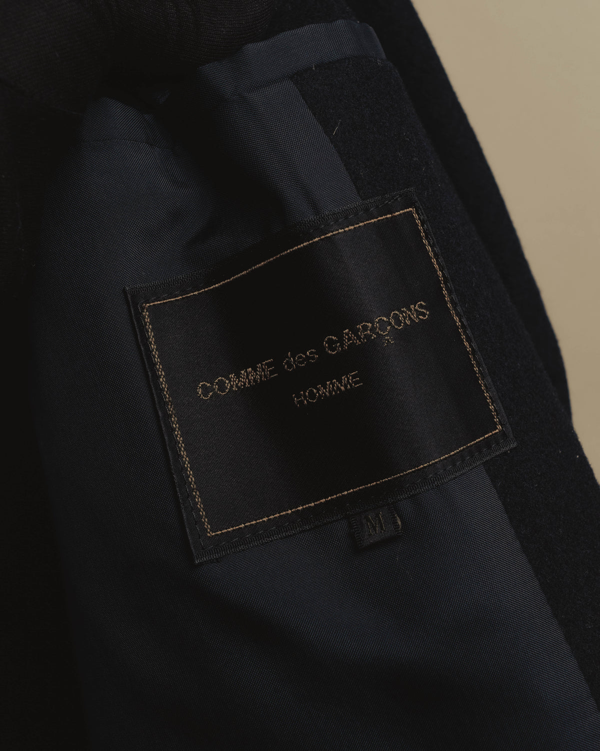 内側のキュプラ裏地に配された「COMME des GARÇONS HOMME」の旧織りネームと、Mサイズ表記を捉えたカット。ブランド名の語順を確認できる内タグです。