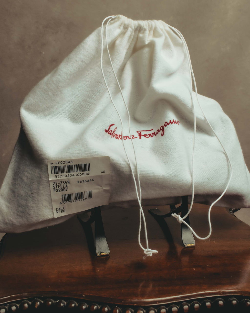 Salvatore Ferragamoの赤い刺繍ロゴが入る巾着型の保存袋と、AQ-217359／STELLA／CALF NEROの表記を確認できる紙タグのカット。