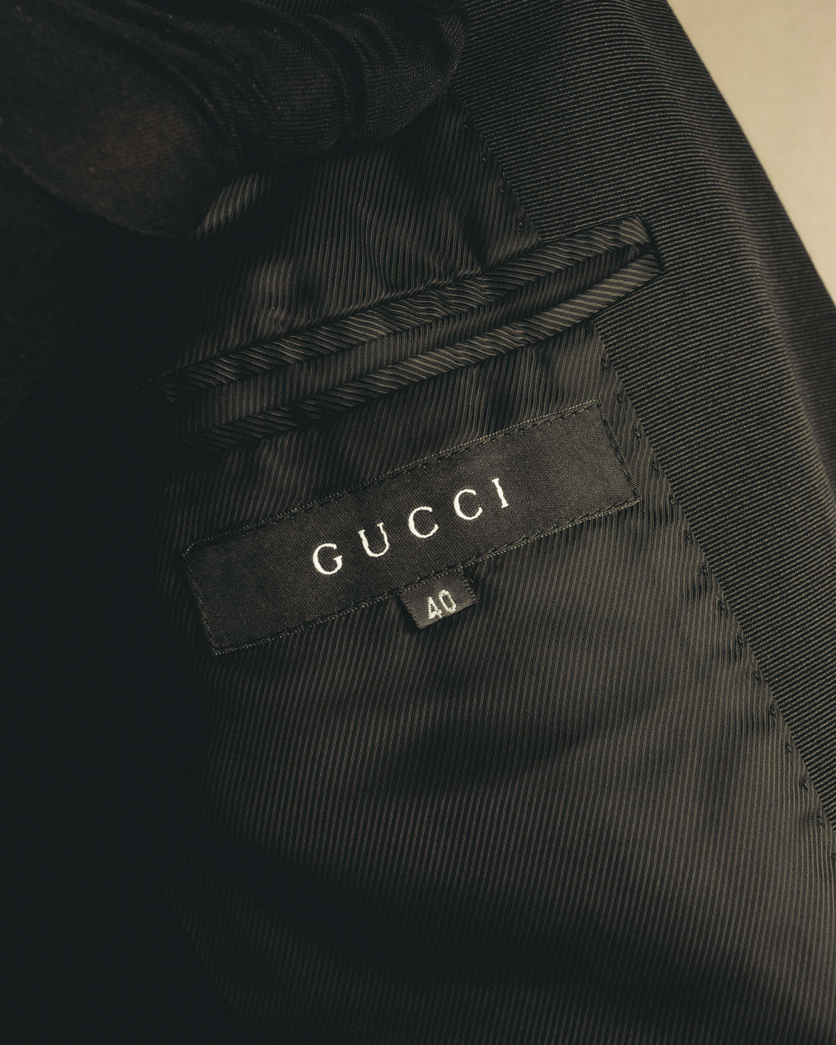 総裏仕立ての内側、襟元に配されたGUCCIのブランドタグとサイズ40表記を捉えたカット。滑らかなレーヨン裏地とチェーン式ハンガーループも確認できます。