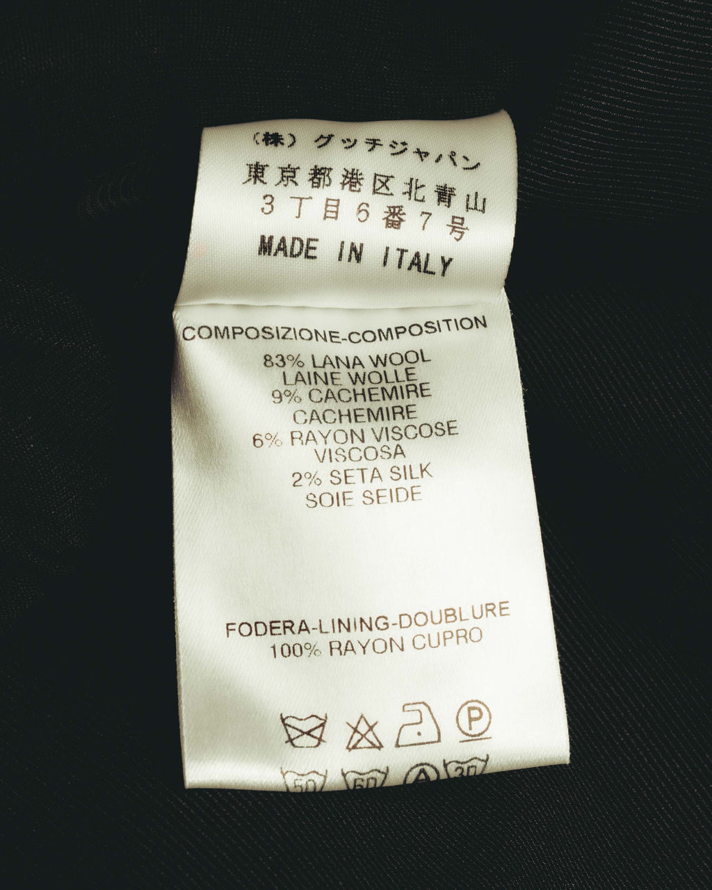 グッチジャパンの北青山3丁目6番7号の所在地表記と「MADE IN ITALY」を確認できる内タグ。表地のウール83%・カシミヤ9%・レーヨン6%・シルク2%、裏地レーヨン100%の混率および洗濯表示を掲載。