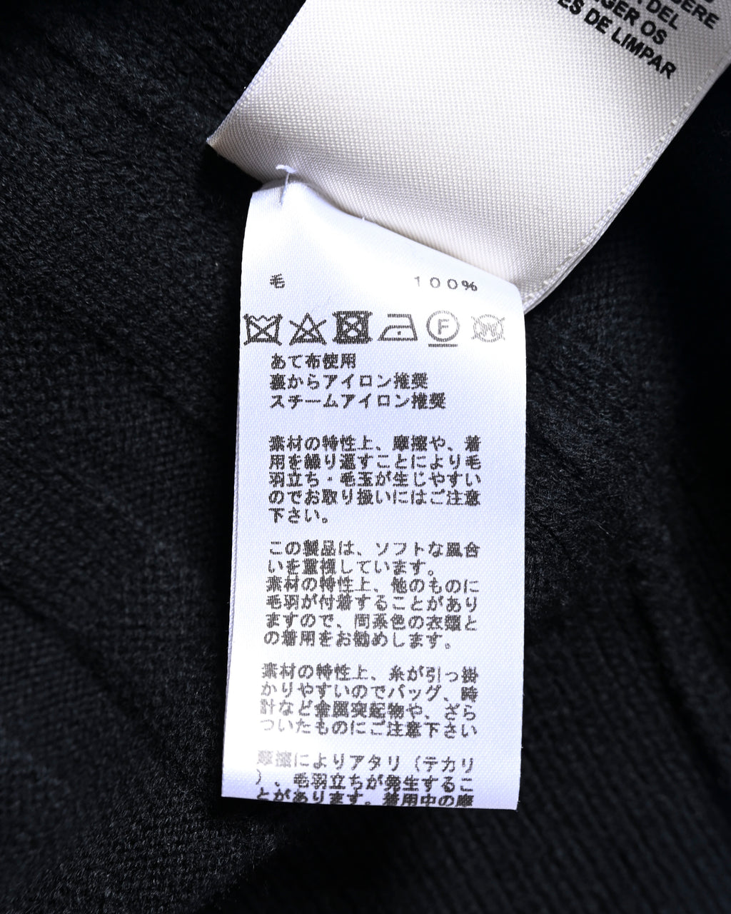 ブラックのニット地に付属する洗濯表示タグのクローズアップ。毛100%表記と、洗濯・アイロンに関するケア表示を確認できるカット。