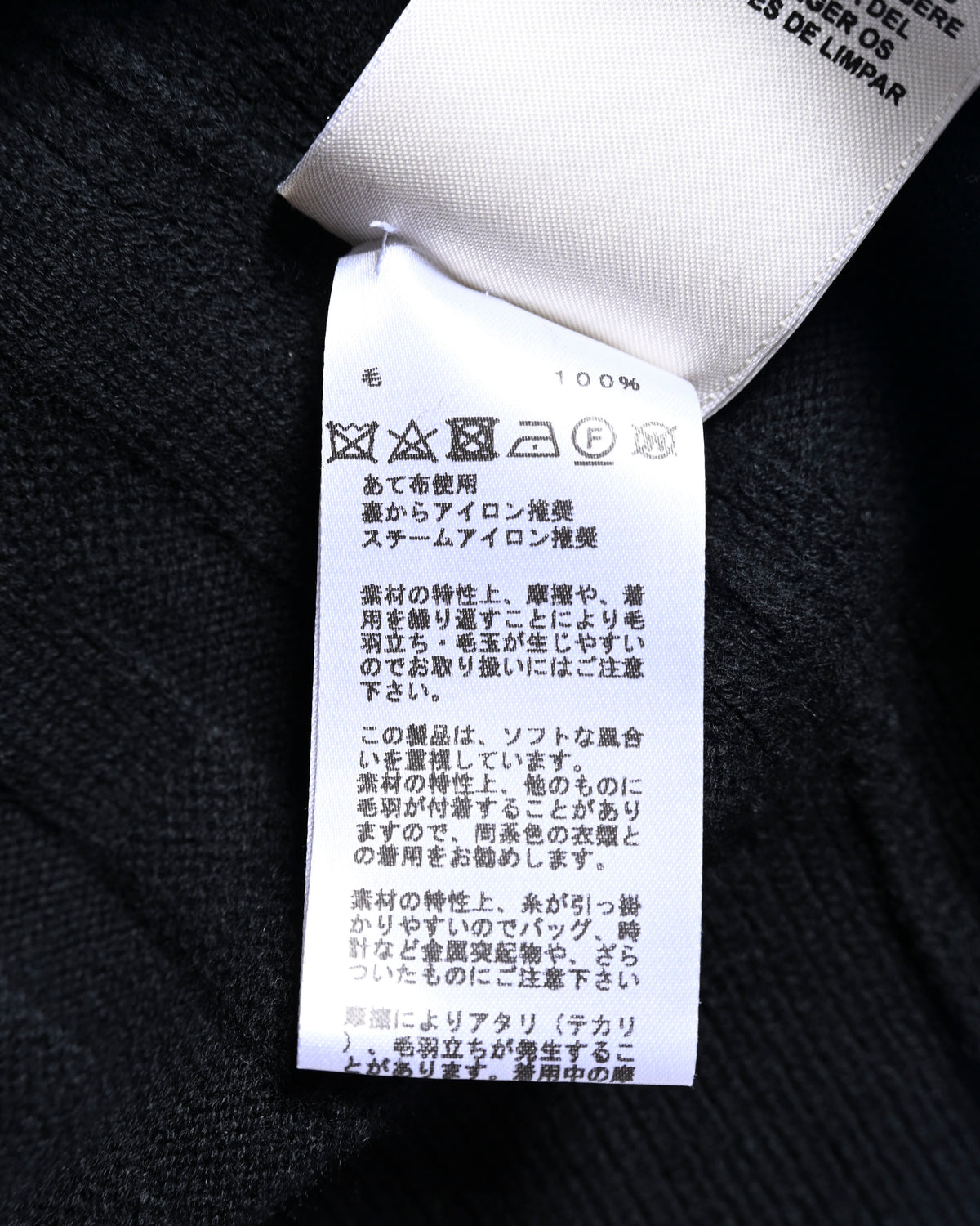 ブラックのニット地に付属する洗濯表示タグのクローズアップ。毛100%表記と、洗濯・アイロンに関するケア表示を確認できるカット。