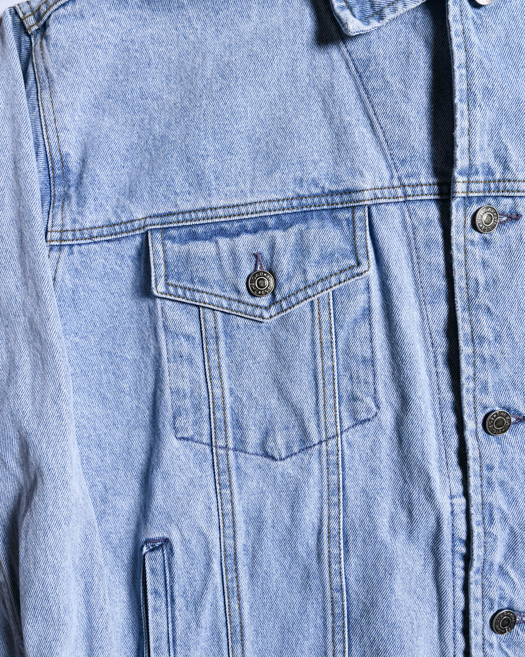 フロントのシャープなフラップ付き胸ポケットと、身頃を縦に走る切り替え・ステッチを捉えたディテールカット。THE GAPの刻印が入ったタックボタンと、淡いライトブルーに色落ちしたデニム生地が確認できます。
