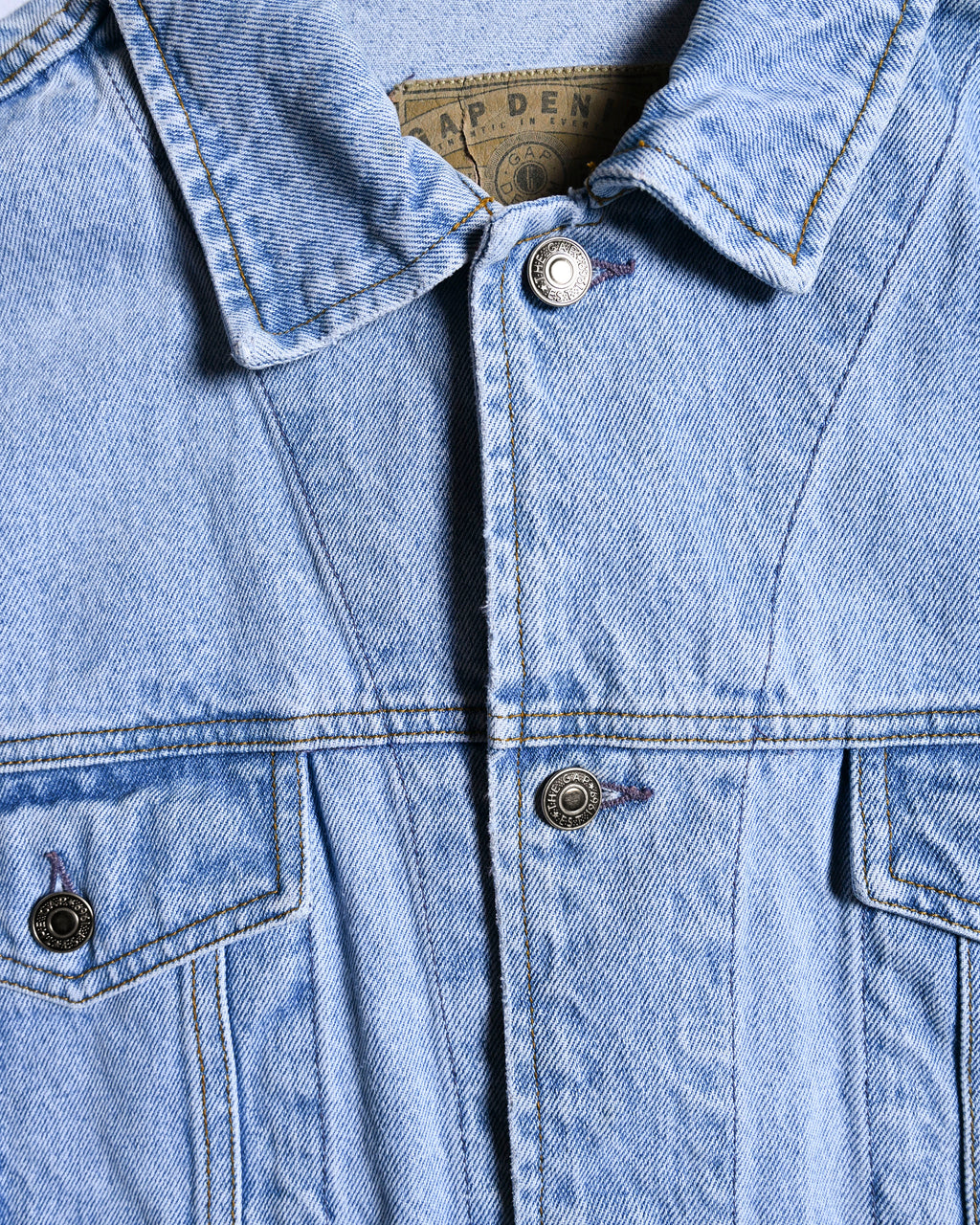 襟裏に残るGAP DENIMのグラフィカルなパッチと、THE GAP・EST. 1969刻印のタックボタンを捉えたフロントディテール。左右対称に配されたシャープなフラップ付き胸ポケットと、身頃を縦に走る切り替え・ステッチも確認できます。