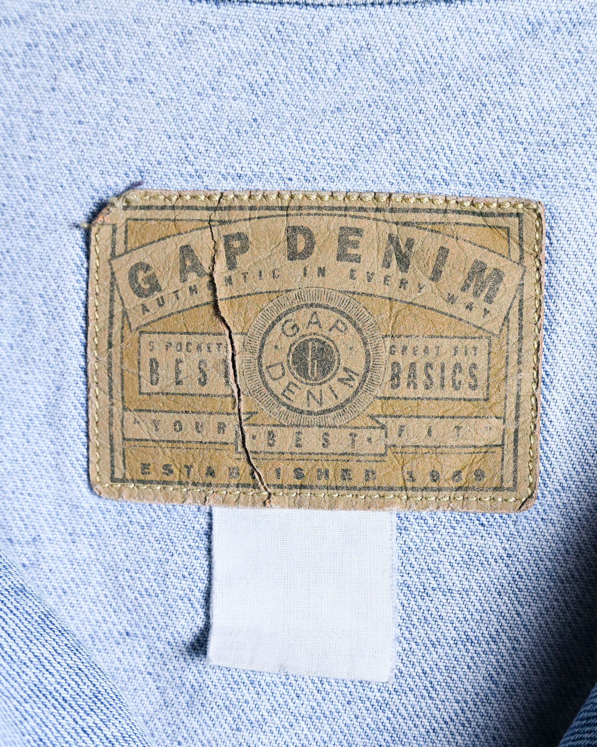 襟裏に残るGAP DENIMのグラフィカルなパッチを捉えたタグカット。パッチ中央に亀裂が生じ、印字には摩耗が見られます。