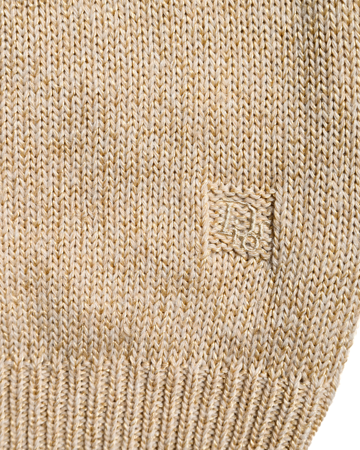 身頃の裾付近に配された、四角い枠で囲まれたCDモノグラム刺繍のディテール。シャンパンベージュの杢調ニットと幅広い裾リブをあわせて確認できるカット。