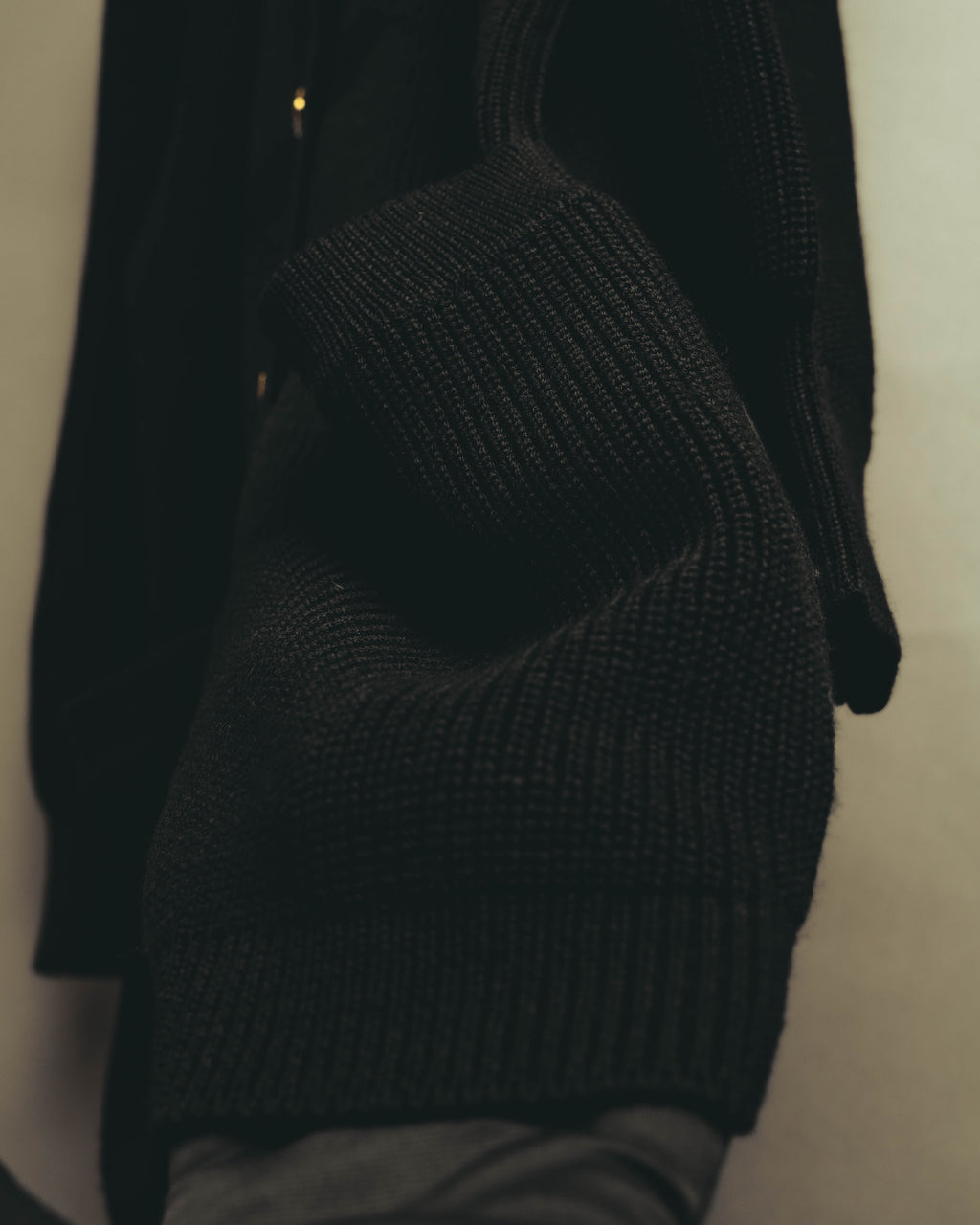 ブラックの畦編みを用いた袖まわりと、長めに設けられた袖口リブの素材感が分かるカット。ゆとりを持たせた袖幅から袖口へ向かう編み地の抑揚を捉えています。