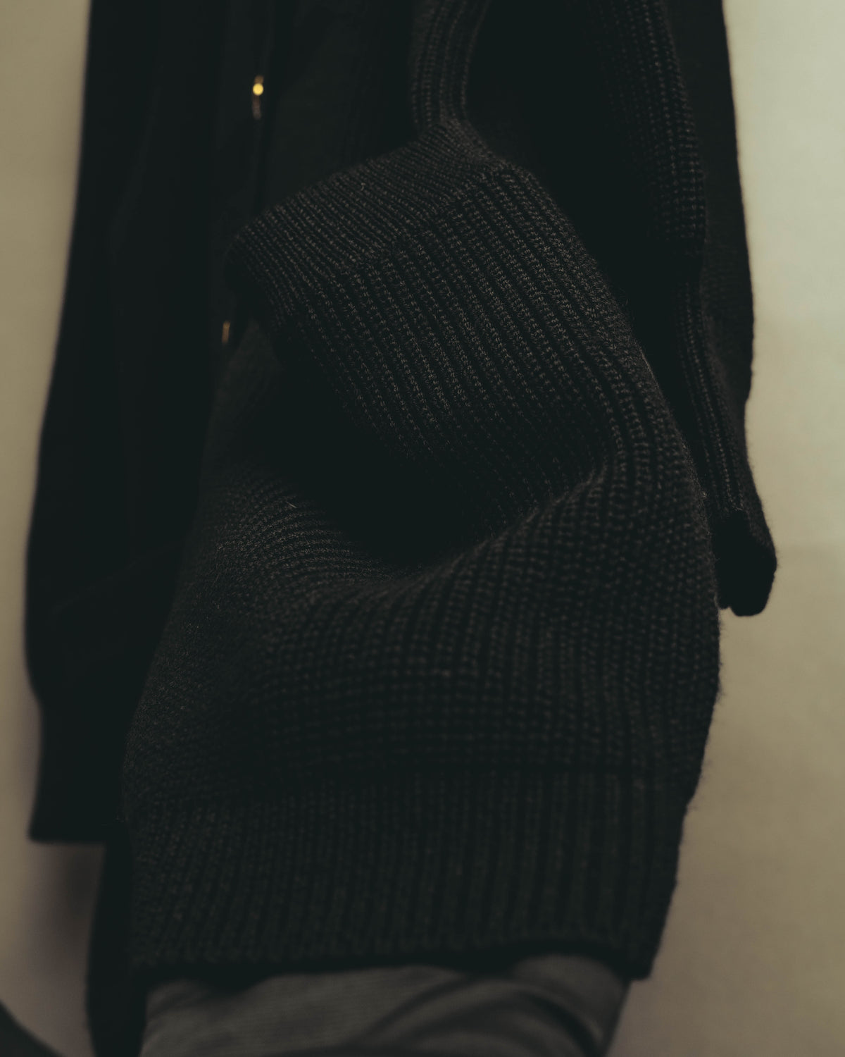 ブラックの畦編みを用いた袖まわりと、長めに設けられた袖口リブの素材感が分かるカット。ゆとりを持たせた袖幅から袖口へ向かう編み地の抑揚を捉えています。