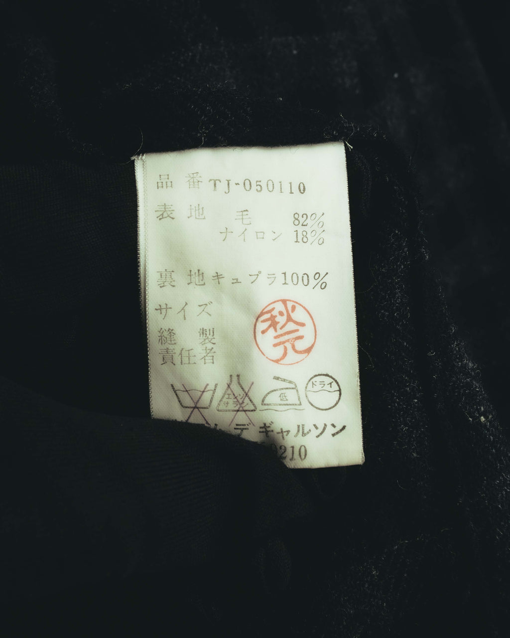 品番TJ-050110と、表地ウール82％・ナイロン18％、裏地キュプラ100％の素材表記が読める内側の品質表示タグ。日本語主体の洗濯表示も確認できるカットです。
