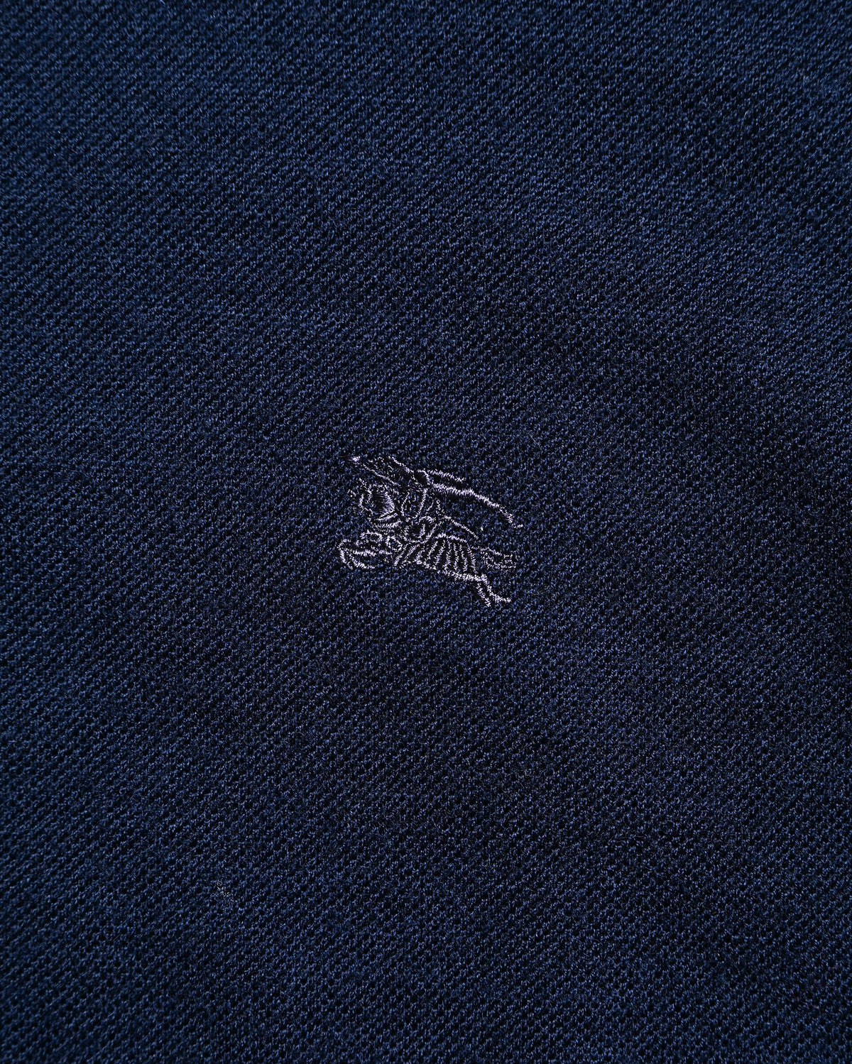 深みのあるネイビーのウールニットボディに施された、トーン・オン・トーンのホースマーク刺繍。ハイゲージの美しい目面とともに確認できる左胸のディテールカット。