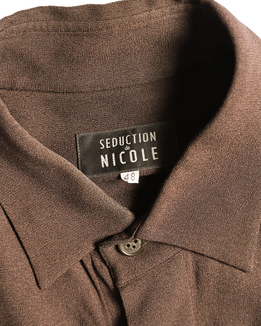 黒地に白文字で表現された「SEDUCTION de NICOLE」の織りネームと、サイズ表記48を確認できる襟元のカット。シャープなレギュラーカラーと第一ボタンも写しています。