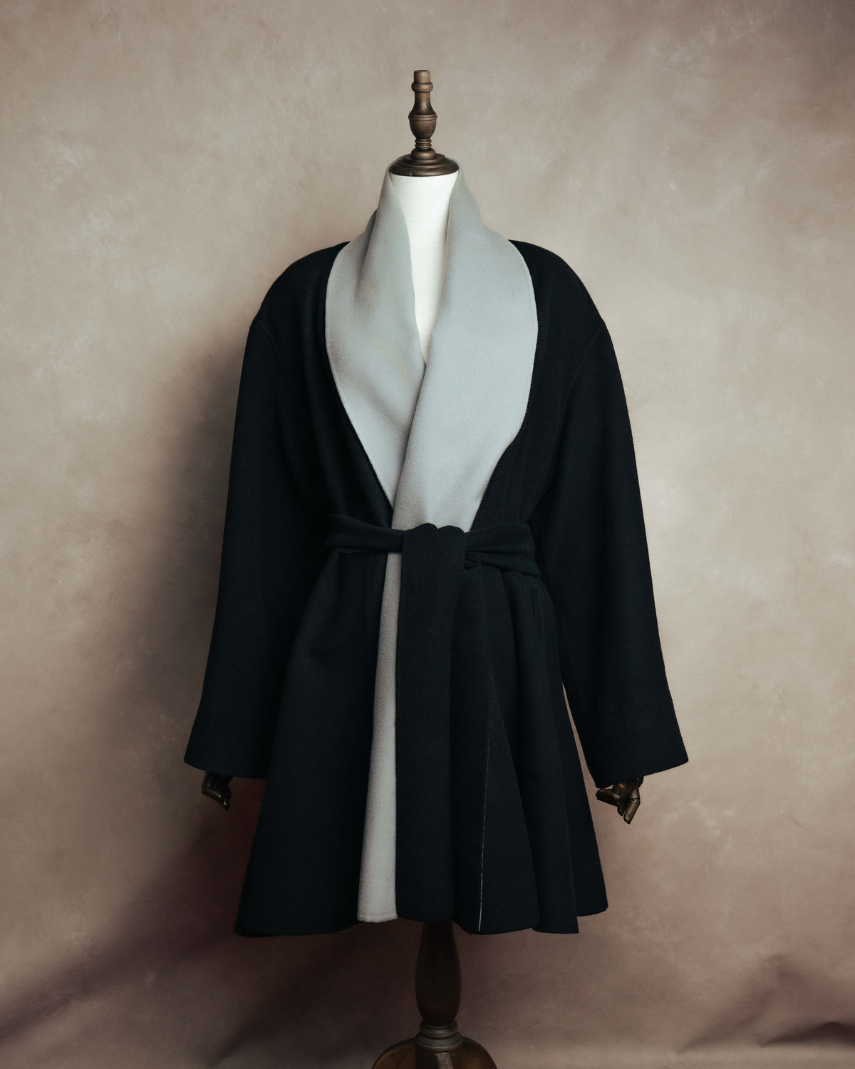 ブラックの身頃に淡いグレーのロングショールカラーを配した、コート前面の全体像。共布ベルトを結んだウエストから裾へ広がるAライン調のシルエットが確認できます。