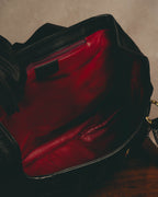 鮮やかな赤から深いマゼンタを思わせる滑らかな内装と、開口部内側に備えたファスナーポケットを捉えたディテールカット。ブラックレザーの外装との色彩のコントラストが分かる一枚です。